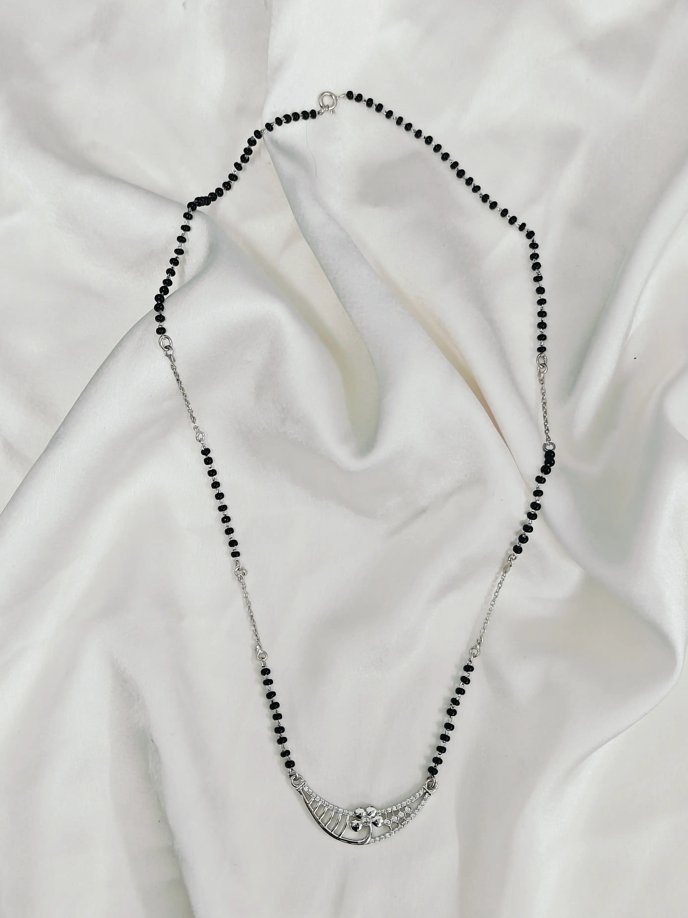 Necklace with black beads and silver clasp on a white fabric background